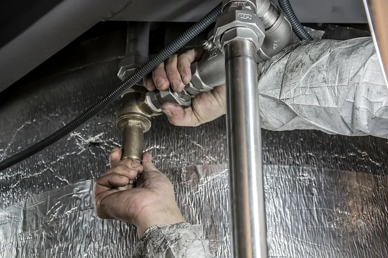 Hände arbeiten an Messingarmaturen und Edelstahlrohren einer gedämmten Rohrleitung
